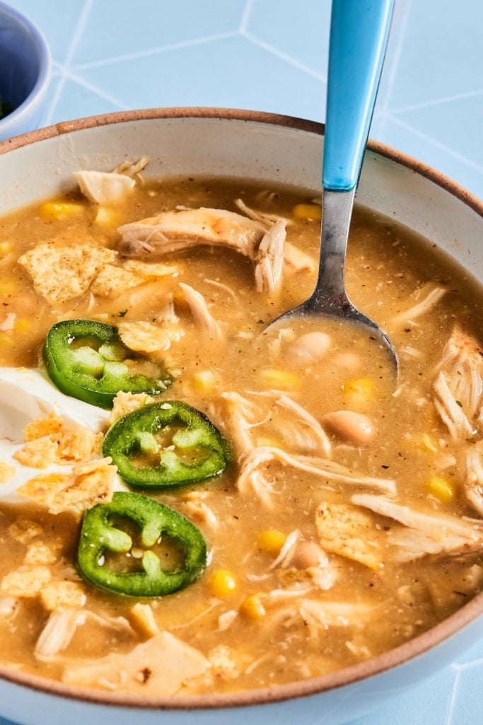 Bowl of white chicken chili with a spoon and fresh garnishes