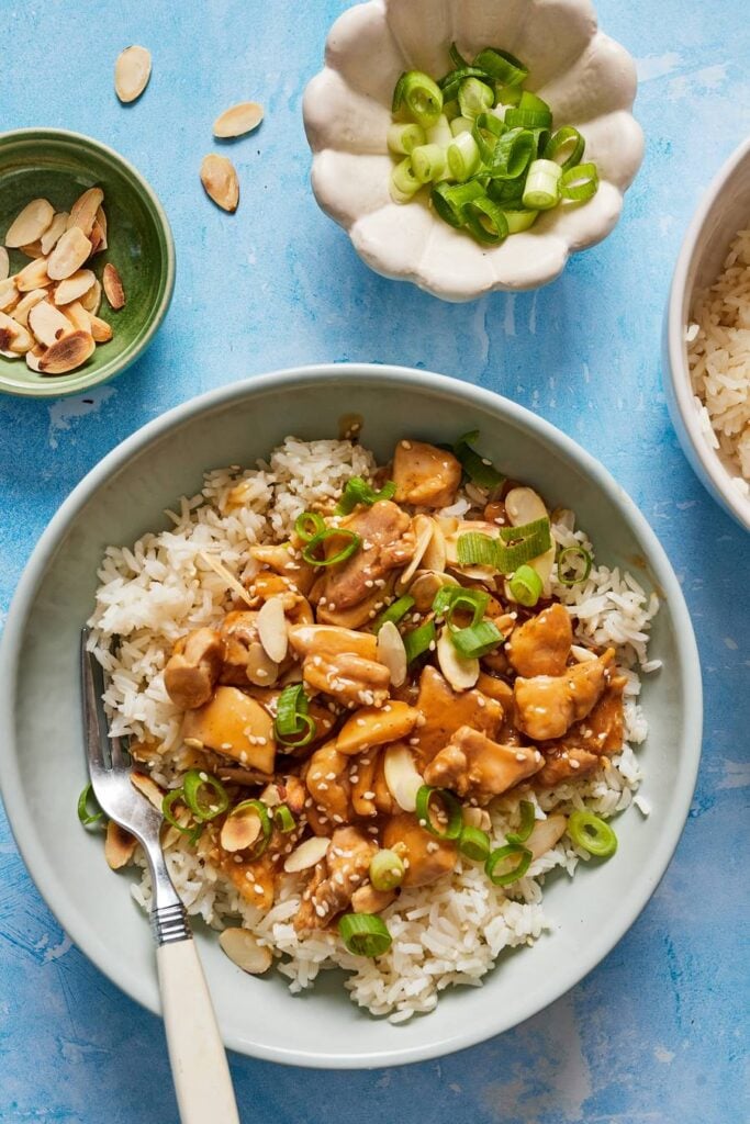 bowl of almond chicken stir fry with green onion garnish on blue background
