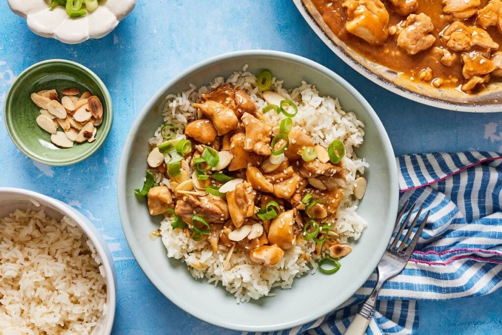 bowl of almond chicken stir fry over rice on a blue background