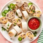 plate of taco tortilla roll ups with salsa for dipping and jalapeno garnish